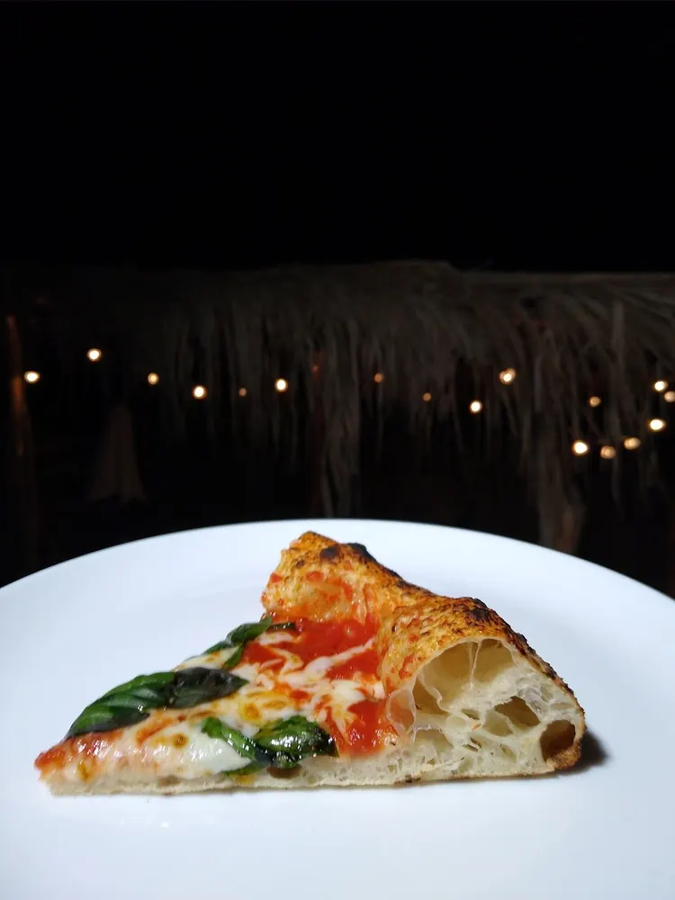 Porción de pizza Margherita con las luces de la terraza de noche